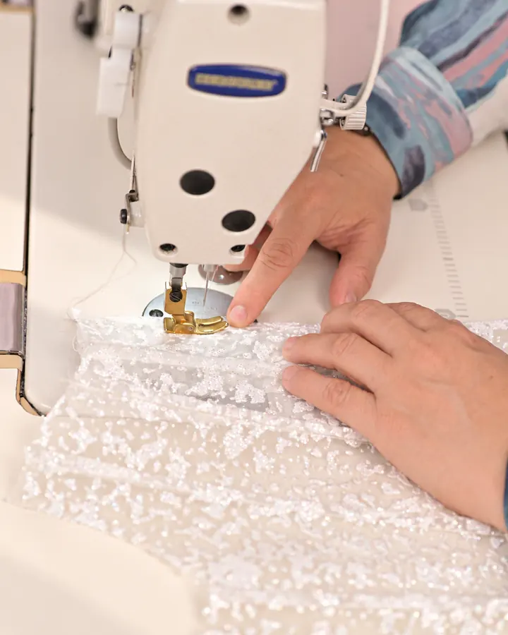 Las manos de Kita guían un encaje blanco en la máquina de coser